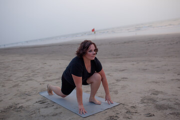 A beautiful plus size woman wearing black sports shorts and a T-shirt doing yoga on the beach