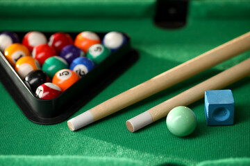 Many colorful billiard balls in triangle rack, cues and chalk on green table, closeup