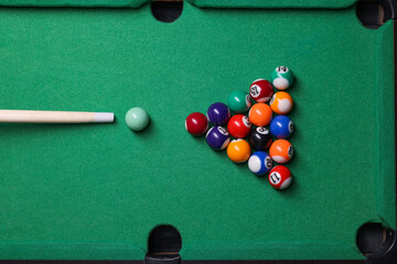 Billiard balls in triangle and cue on green table, top view