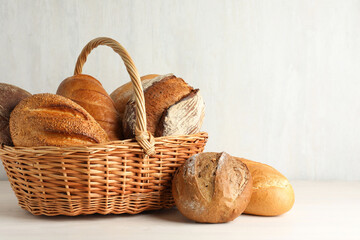 Different freshly baked bread loafs and wicker basket on white wooden table, closeup. Space for text