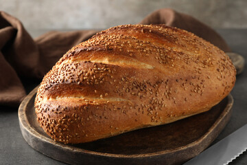 Freshly baked bread with seeds and knife on grey table, closeup