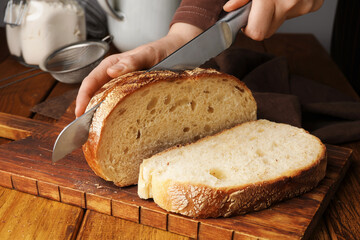 Woman cutting freshly baked bread at wooden table, closeup