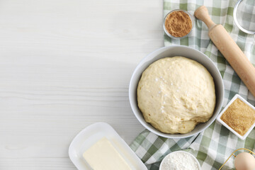 Making cinnamon rolls. Fresh dough in bowl, ingredients and rolling pin on light wooden table, flat lay. Space for text