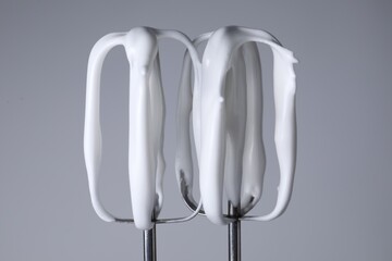 Whisks with whipped cream on light grey background, closeup
