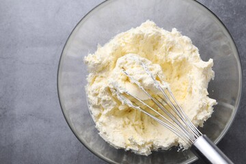 Bowl with whisk and whipped cream on grey table, top view