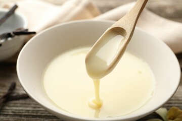 Taking tasty vanilla condensed milk with spoon from bowl on wooden table, closeup