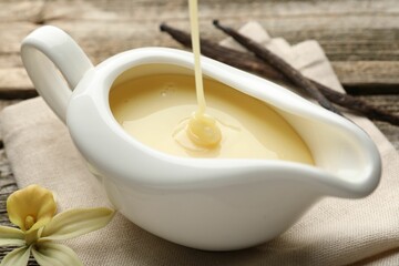 Pouring tasty vanilla condensed milk into gravy boat on wooden table, closeup