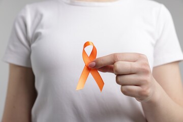 Multiple Sclerosis awareness. Young woman holding orange ribbon on light grey background, closeup