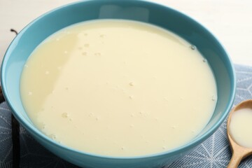 Tasty vanilla condensed milk and spoon on white table, closeup