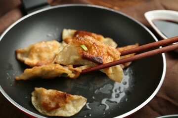 Taking tasty fried gyoza (dumpling) with chopsticks on wooden table, closeup