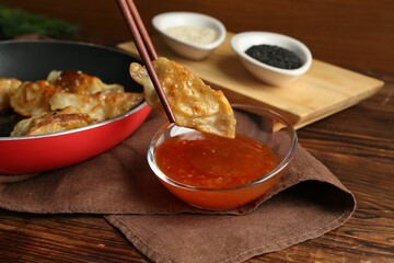 Dipping tasty fried gyoza (dumpling) into sauce on wooden table, closeup