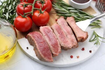 Delicious sliced beef tenderloin with different degrees of doneness, tomatoes, spices and oil on light table, closeup