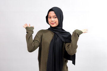 Indonesian woman in a black hijab and olive green sweater, smiling slightly while raising both...
