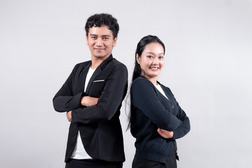 Asian man and woman standing back-to-back with arms crossed, smiling confidently. Both wear black blazers over white shirts, showing teamwork, success, and professional confidence.