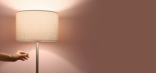 Woman turning on floor lamp near pink wall. Banner for design