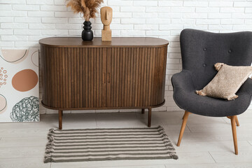 Stylish interior of living room with drawers, armchair, painting and soft rug