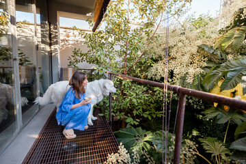 A woman in a relaxed blue outfit enjoys a quiet moment with her fluffy white dog on a lush green...