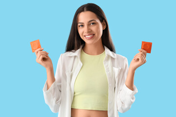 Young woman with condoms on blue background
