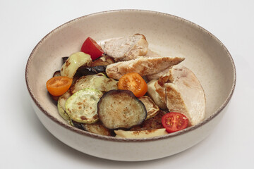 The image shows a bowl filled with a variety of grilled and roasted vegetables, along with sliced pieces of chicken. 
