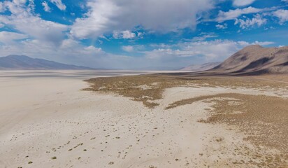 Aerial view of the Black Rock Desert playa in Nevada, USA. The dry lakebed stretches to the horizon, surrounded by mountains under a partly cloudy sky.  Gerlach, Nevada, USA