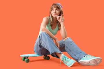 Young woman with skateboard sitting on orange background