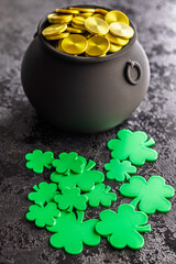 St. Patrick's Day. Green clover leaves decoration and cauldron with golden coins on black table.