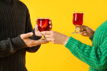 Young couple with glasses of mulled wine on yellow background, closeup