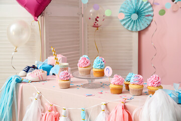 Delicious cupcakes with baby booties and decorations on table against pink background. Gender...