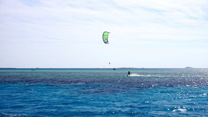 A kitesurfer is soaring above the clear waters of the Red Sea on a sunny summer day. With a bright blue sky and turquoise sea, this scene is perfect for travel, adventure, and watersports content. 