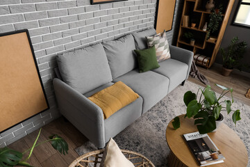 Interior of modern living room with cozy grey sofa and coffee table near brick wall