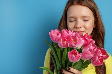 Fototapeta premium Beautiful teenage girl with bouquet of tulips on light blue background, space for text