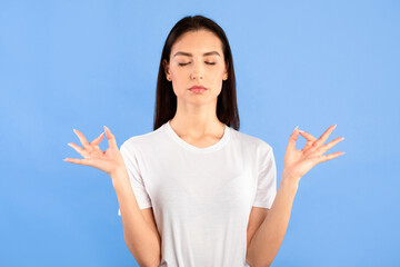 Calm Down. Peaceful young woman practicing breathing yoga exercise with closed eyes, blue studio...