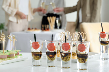 Many different tasty canapes on white table. People clinking glasses of wine indoors, closeup