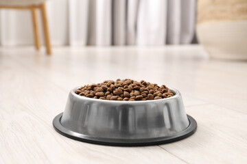 Dry pet food granules in feeding bowl on floor indoors