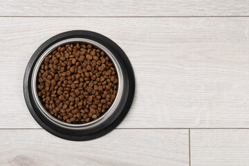 Dry pet food granules in feeding bowl on floor, top view. Space for text