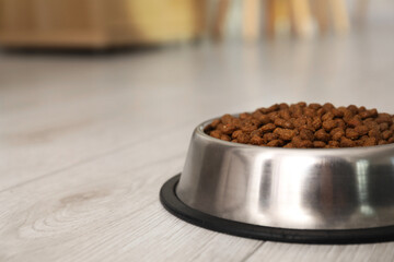 Dry pet food granules in feeding bowl on floor indoors, space for text