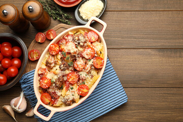 Delicious pasta casserole in baking dish with ingredients on wooden table, flat lay. Space for text