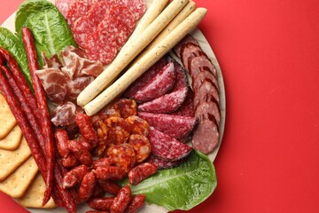 Different smoked sausages and other snacks on red background, top view. Space for text