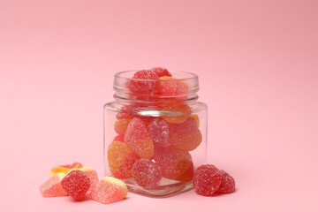 Tasty jelly candies in glass jar on pink background, closeup