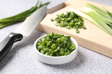 Fresh green onions and knife on light grey table, closeup