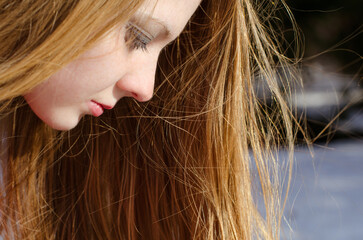 Close-up of young female with long blonde hair and fair skin, gazing downwards in snowy landscape....
