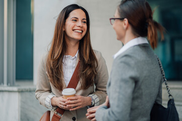Two businesswomen having a coffee break and chatting outside office