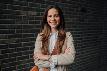 Smiling businesswoman posing with crossed arms in front of brick wall