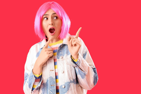 Shocked young woman in wig pointing at something on red background. Accusation concept