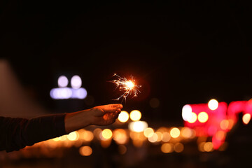 Burning sparkler against blurred lights of city at night