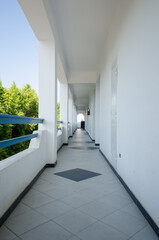 Long hotel corridor with white walls and tiled floor under bright natural light. Corridor leads to...