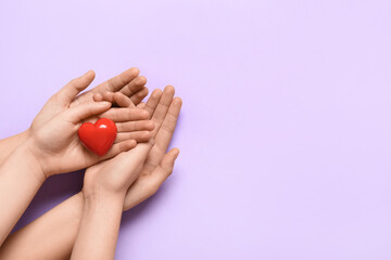 Hands of woman and child with red heart on lilac background