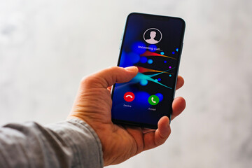 Close-up of a hand holding a smartphone with an incoming call screen. Display shows Incoming call...