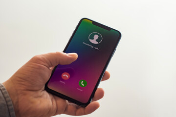 Close-up of a hand holding a smartphone with an incoming call screen. Display shows Incoming call with green accept and red decline buttons.