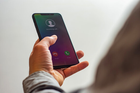 Close-up of a hand holding a smartphone with an incoming call screen. Display shows Incoming call with green accept and red decline buttons.